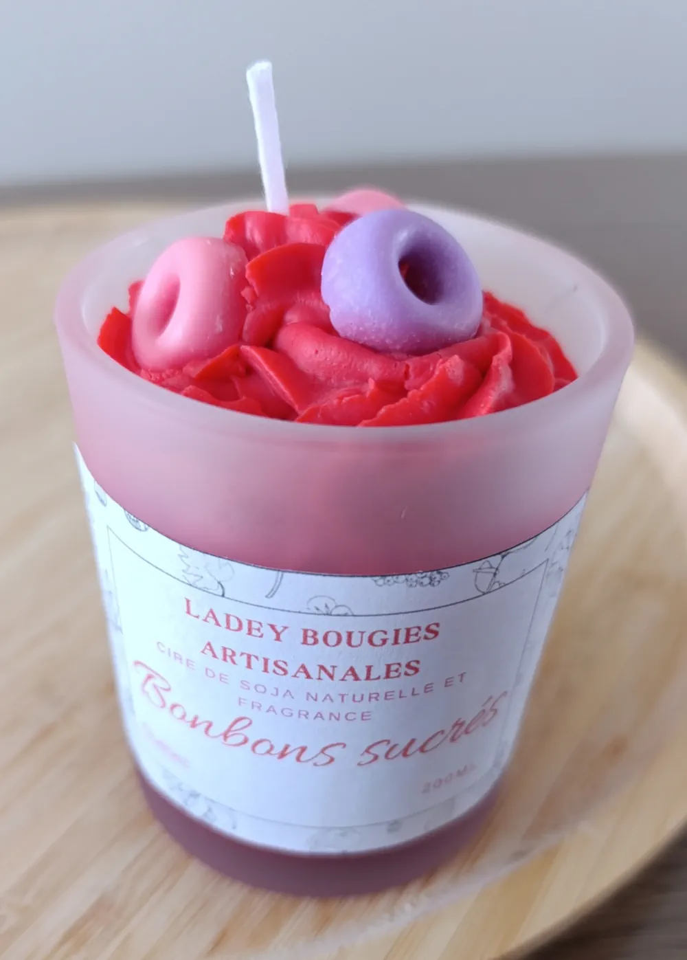 Bougie artisanale dans un verre givré de 200ml bonbons sucrés, coiffée d’une cire rouge en forme de crème fouettée et décorée de minis beignes (donuts) en cire rose et violette.