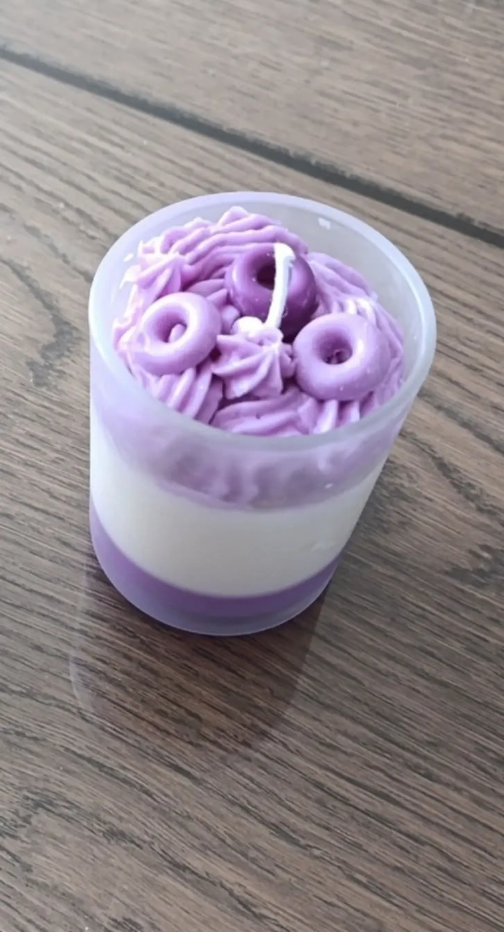 Bougie artisanale dans un verre givré de 200ml au parfum amande et vanille, composée de couches de cire violette et blanche, surmontée d’un décor de cire violette en forme de volute et de minis donuts autour de la mèche.