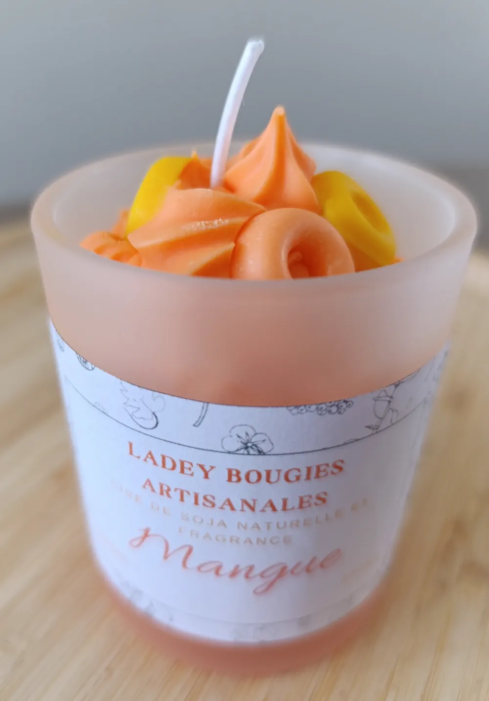 Bougie artisanale dans un verre givré de 200ml au parfum mangue, ornée d’un tourbillon de cire orange et jaune façon crème fouettée.