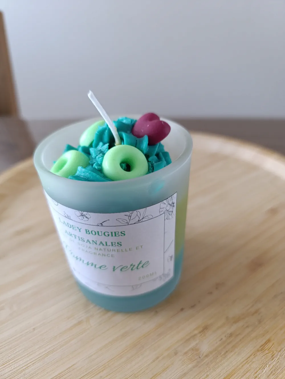 Bougie artisanale dans un verre givré de 200ml au parfum pomme verte, remplie de cire turquoise et décorée de minis donuts verts et d’un cœur rouge en cire
