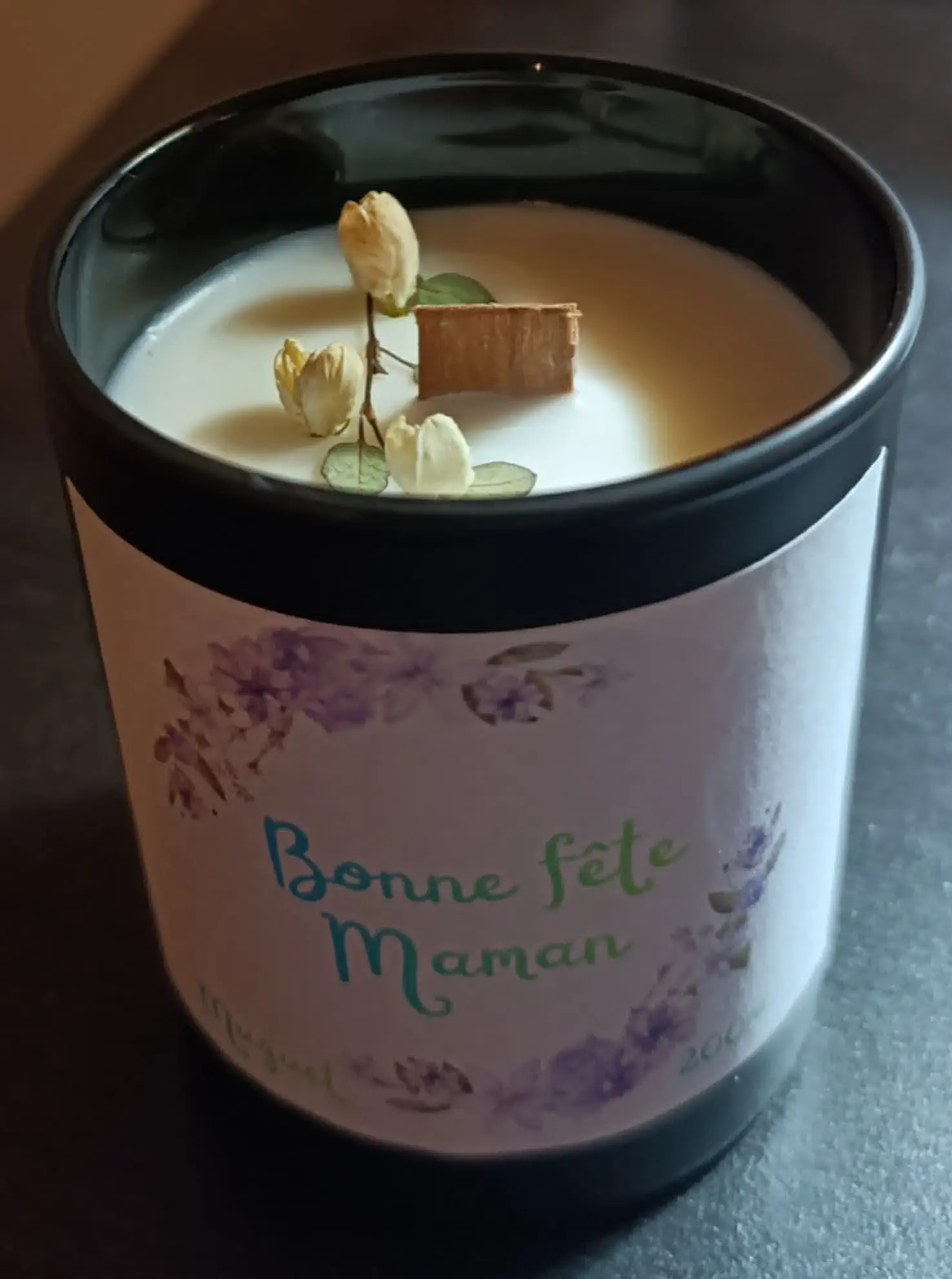 Bougie artisanale dans un verre noir satiné de 200ml, au parfum doux et floral, composée d’une cire blanche lisse parsemée de petites fleurs séchées, surmontée d’une mèche en bois entourée d’un délicat décor botanique.